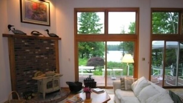 A living room with a fireplace, a white sofa, a coffee table, and large windows overlooking a garden.