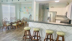 A kitchen with white cabinets, a stainless steel refrigerator, and a bar area with stools.