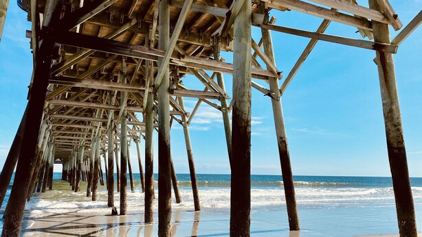 A wooden pier structure extending into the ocean with a clear sky above.