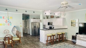 A kitchen with white cabinets, a stainless steel refrigerator, a microwave, and a large island with bar stools.