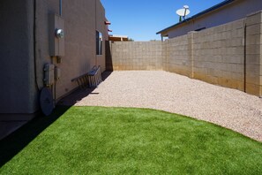 outdoor space with artificial grass and gravel surface, enclosed by a low brick wall.