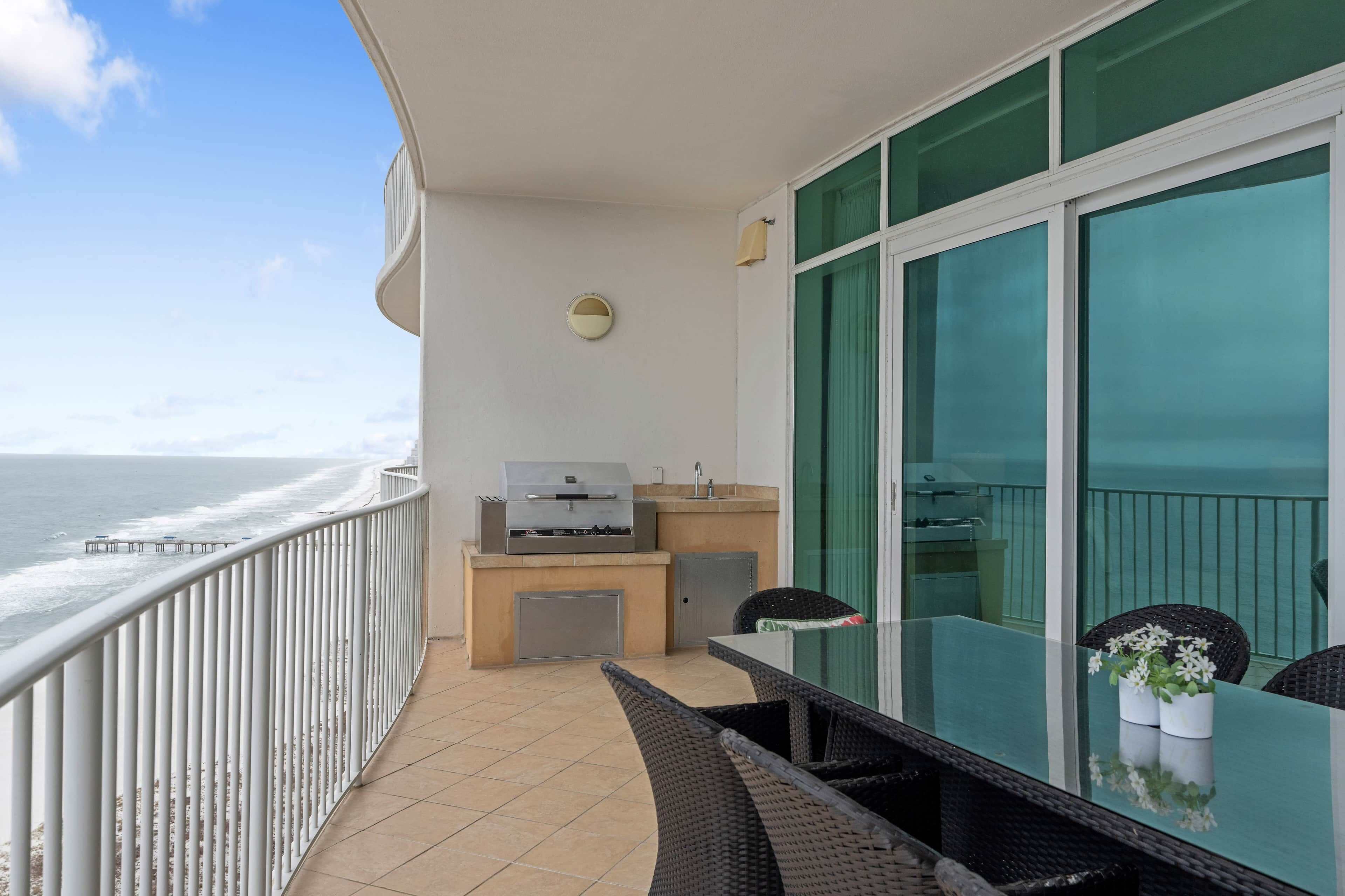 A balcony with a view of the ocean, a grill, and a table with chairs.