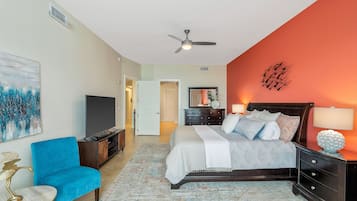 A bedroom with a bed, a blue armchair, a TV, and a ceiling fan.