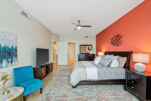 Un dormitorio con cama, un sillón azul, televisor y ventilador de techo.