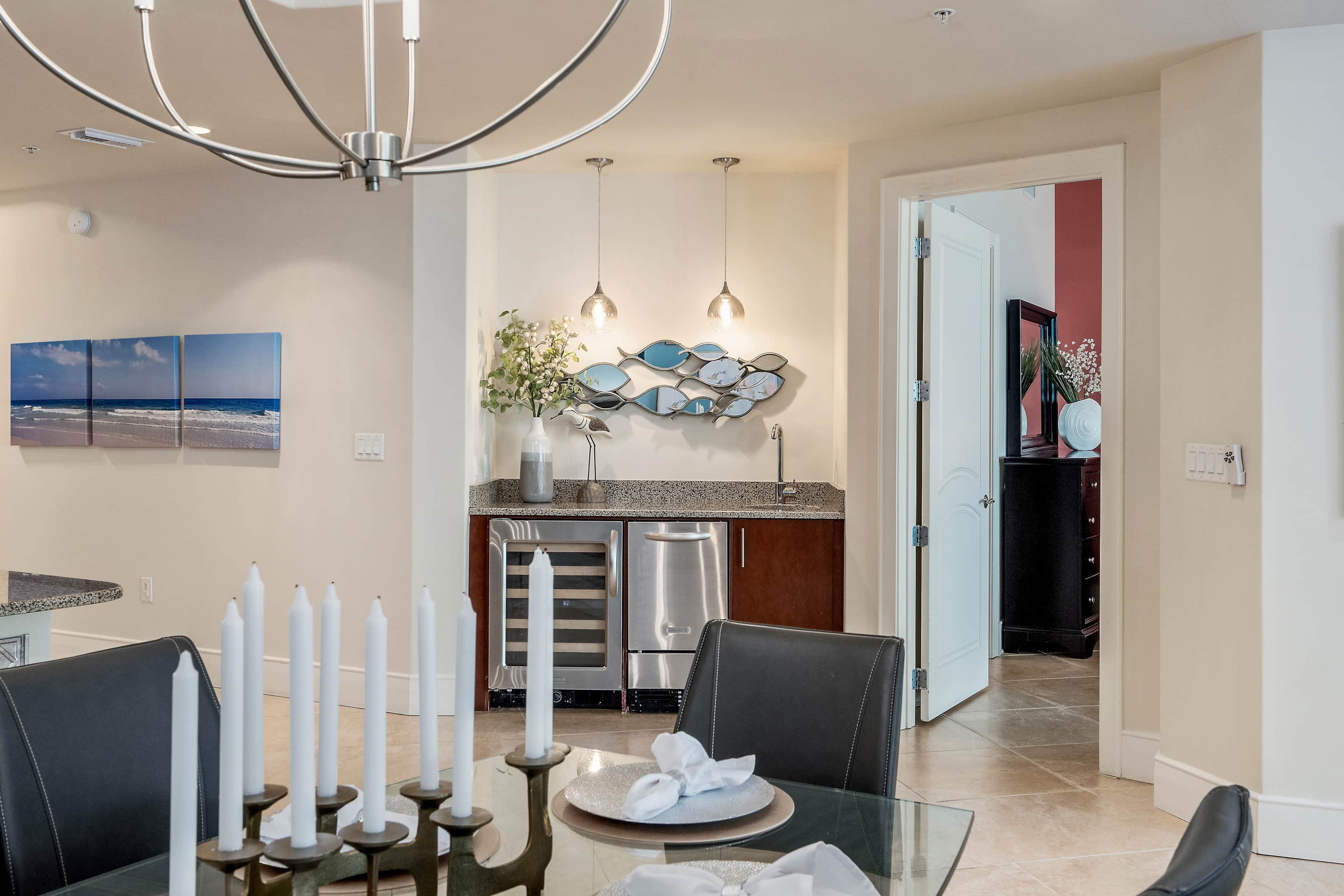 A dining area with a glass table, candles, and a view of the kitchen and living area.