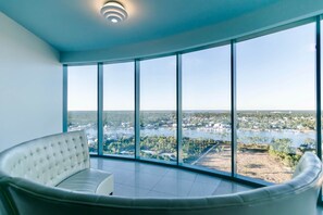 A spacious room with a large curved white sofa and a panoramic view of a lake and surrounding area through floor-to-ceiling windows. - Ultimate Beachfront Elegance - Turquoise Place C1704 (Orange Beach)