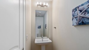 A bathroom with a pedestal sink, a mirror, and a starfish artwork on the wall.
