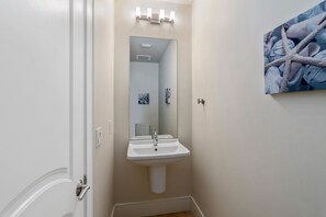 Un baño con lavamanos pedestal, un espejo y una obra de arte con forma de estrella de mar en la pared.