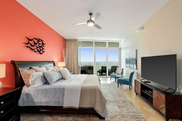 A hotel room with a bed, a television, a ceiling fan, and a view of the ocean.