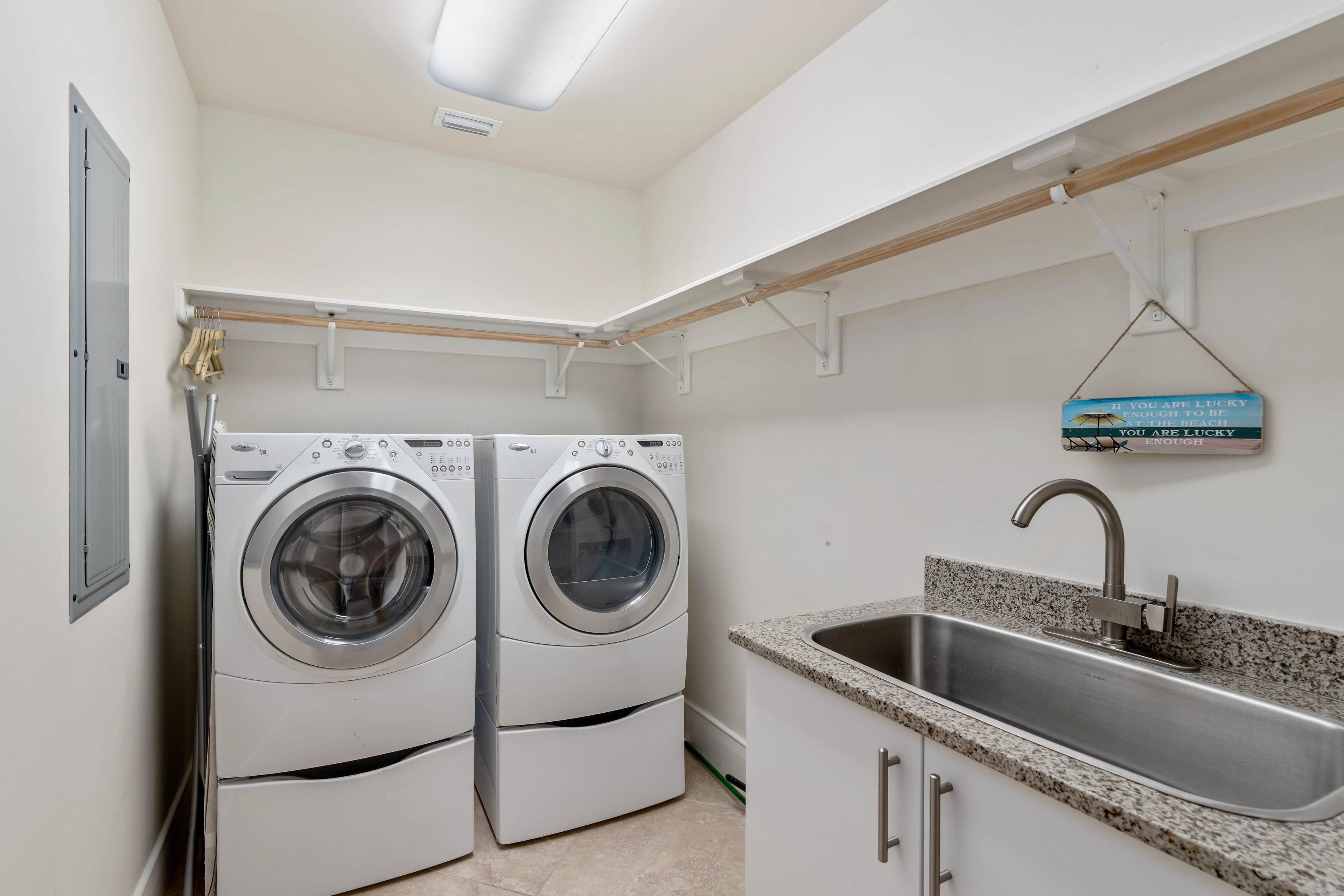 A laundry room with two front-loading washing machines, a stainless steel sink, and a motivational sign.