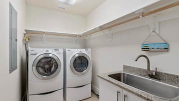 A laundry room with two front-loading washing machines, a stainless steel sink, and a motivational sign.