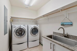 A laundry room with two front-loading washing machines, a stainless steel sink, and a motivational sign.