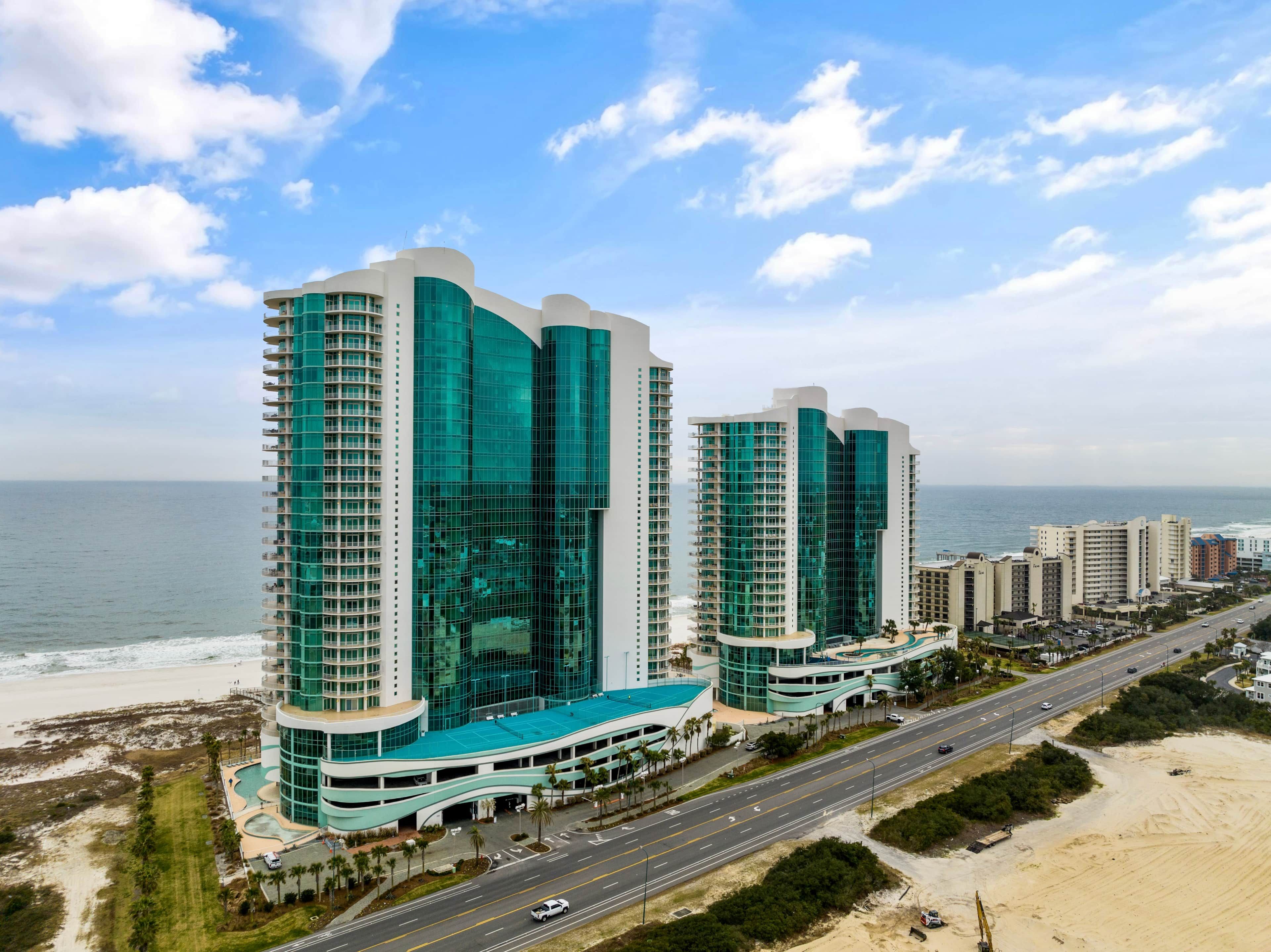 A high-rise hotel with a curved facade, multiple balconies, and a beach view.