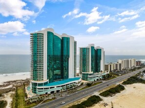A high-rise hotel with a curved facade, multiple balconies, and a beach view.