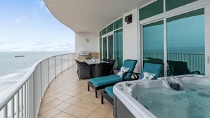 A balcony with a hot tub, seating area, and a view of the sea.