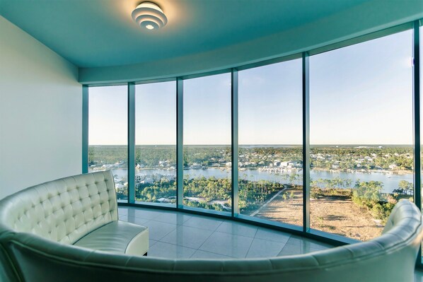 Relax in a spacious room with a curved sofa and floor-to-ceiling windows offering a panoramic view of the surrounding lakeside landscape.