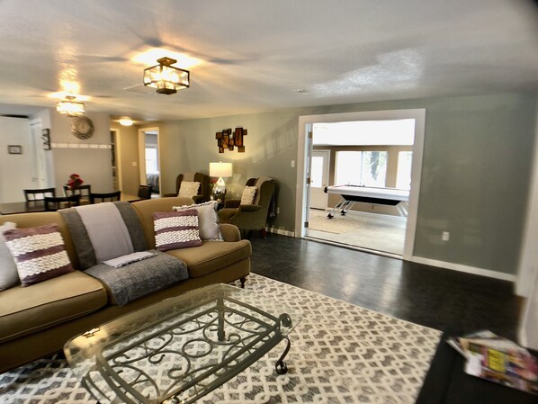 A living room with a sofa, coffee table, and a dining area in the background.