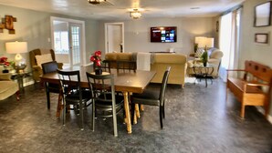 A spacious living area with a dining table, chairs, a sofa, and a TV mounted on the wall. - Amazing Updated Retreat with Fully Stocked All Seasons Game Room!  (St. Helen)