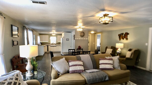 A spacious living room with a sofa, armchairs, and a coffee table. There is a dining area with a table and chairs, and a kitchen in the background. - Amazing Updated Retreat with Fully Stocked All Seasons Game Room!  (St. Helen)