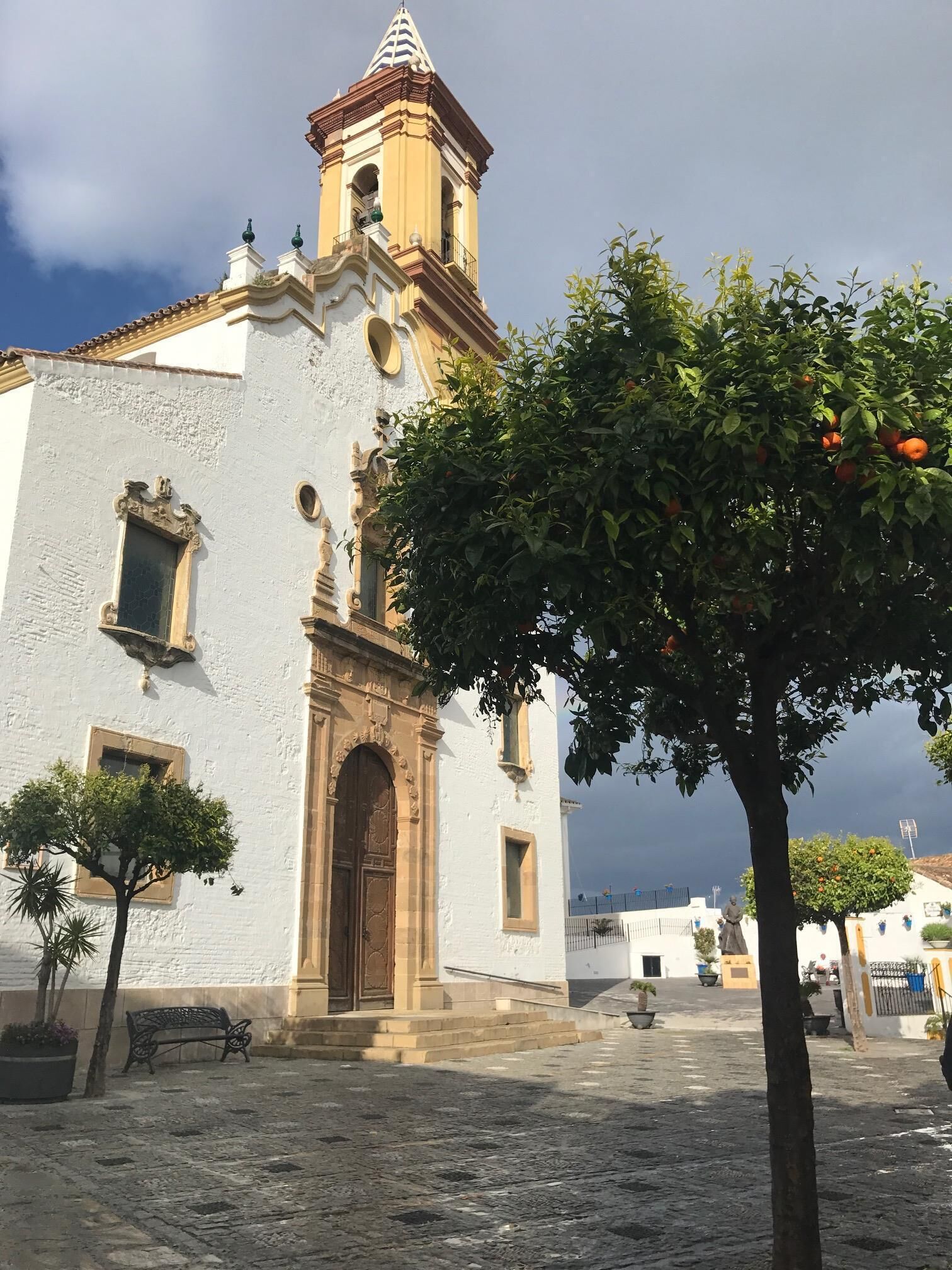 A historic building with a bell tower, arched doorway, and a courtyard with benches and potted plants.