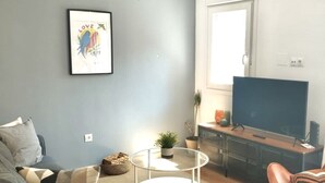 Een woonkamer met een grijze bank, een salontafel, een tv-meubel met een flatscreen televisie en een plafondventilator.