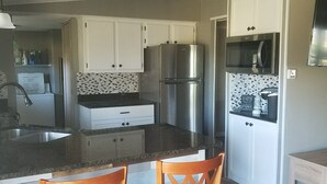 A modern kitchen with white cabinets, a stainless steel refrigerator, and a microwave. There are two wooden chairs at the island.