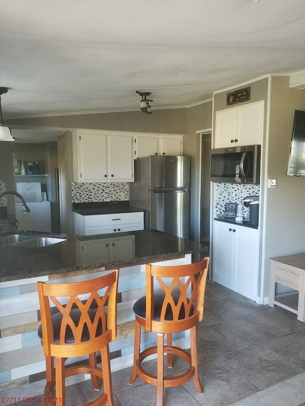 Una cocina moderna con armarios blancos, un refrigerador de acero inoxidable y un microondas. Hay dos sillas de madera en la isla.