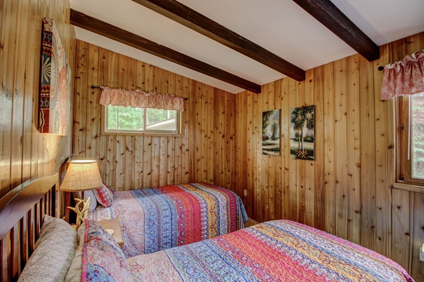 A wooden-paneled room with two beds, a window, and a lamp.
