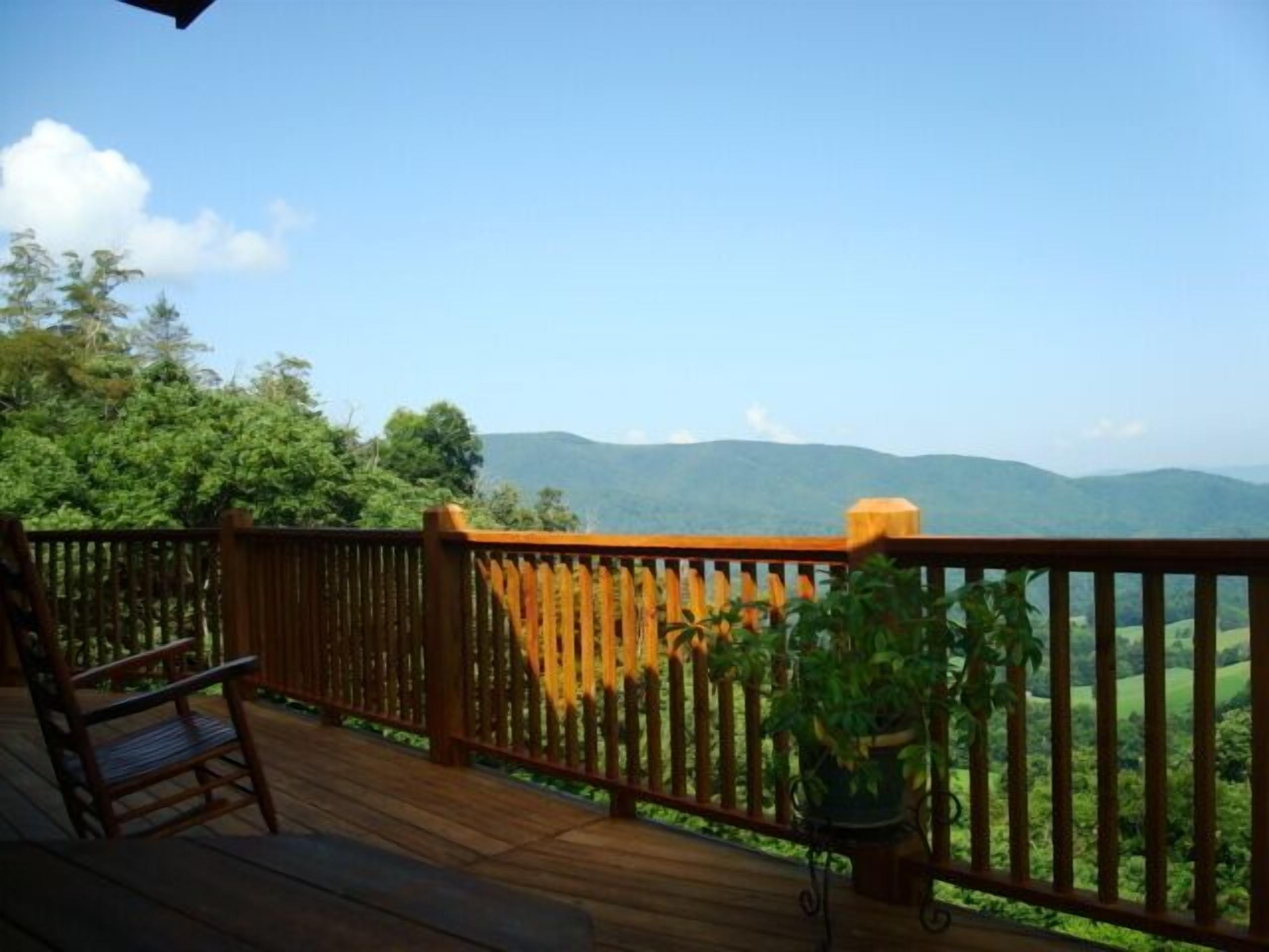 A wooden deck with a railing, a chair, and a potted plant, overlooking a mountainous landscape.