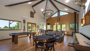 A spacious living area with a pool table, a billiards table, and a fireplace. There are large windows providing natural light and views of the outdoors. - Incredible Mtn Views - 106 Acres: Private Pool, Pickleball Fall of 2026 (Zionville)
