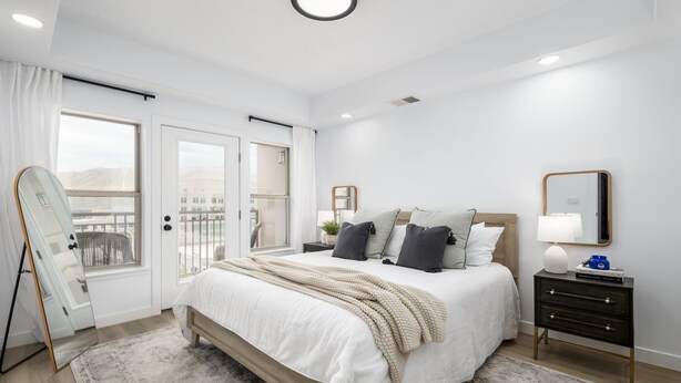 Ein Schlafzimmer mit einem Bett, Nachttischen, einem Spiegel und Blick durch ein Fenster.