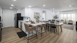 Eine moderne Küche mit weißen Schränken, einem schwarzen Kühlschrank und einem Essbereich mit Korbstühlen und einem Holztisch.