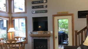 Un salon avec une cheminée, un téléviseur, un coin repas avec des chaises et des panneaux indicateurs sur le mur.
