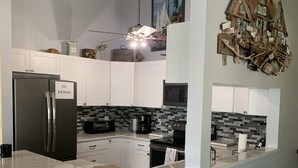 A modern kitchen with white cabinets, a marble countertop, and a built-in stove. There is a refrigerator with a sign indicating "151 3rd Street." A ceiling fan and a decorative wooden piece are also visible.