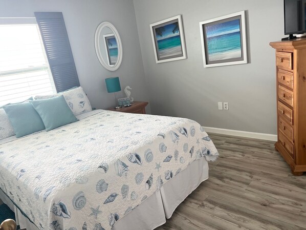 Een slaapkamer met een bed, nachtkastje, kaptafel en twee foto's in lijsten aan de muur.