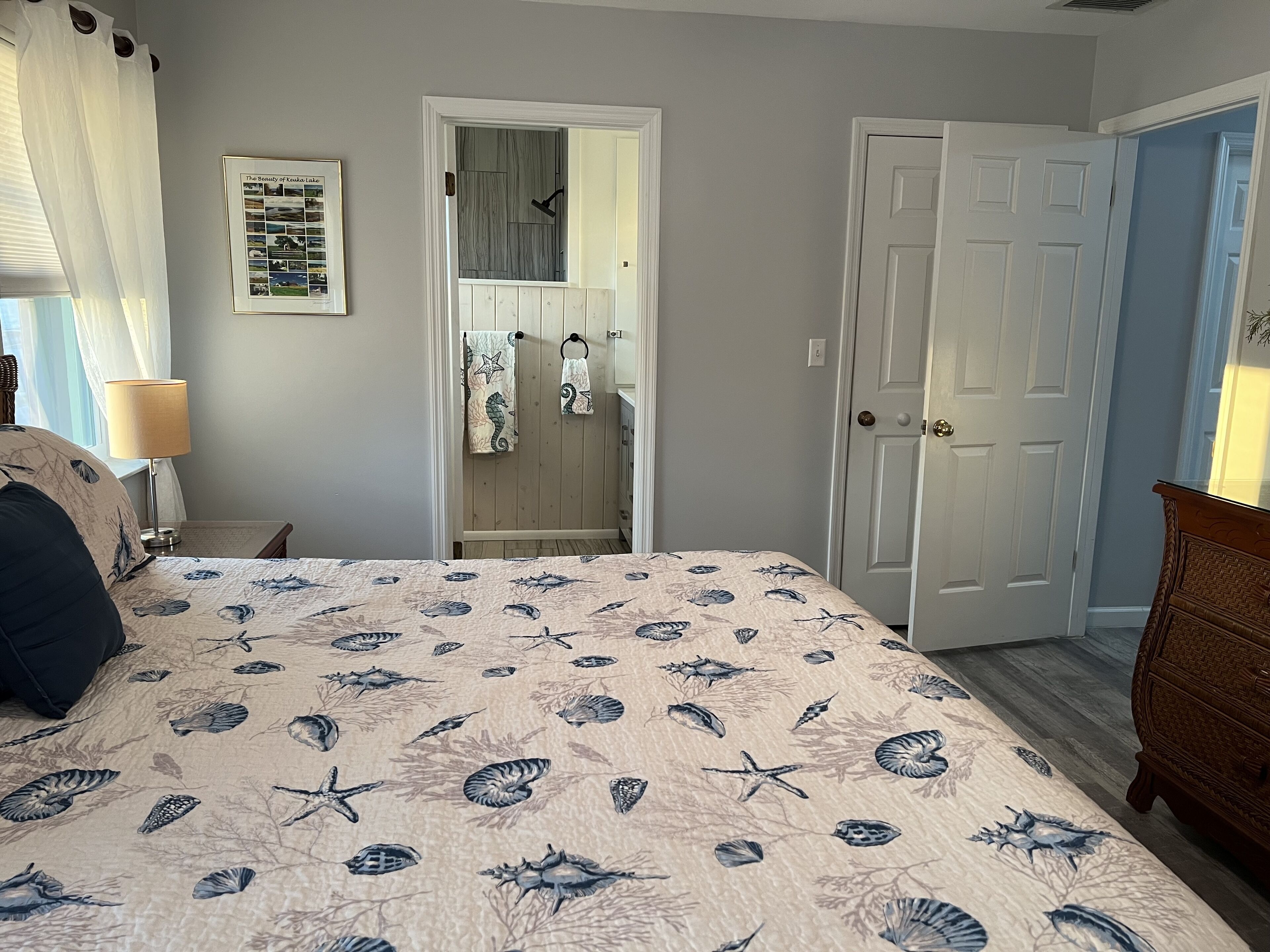 Une chambre à coucher avec un lit, une table de chevet, une commode, une porte et un tableau encadré au mur.