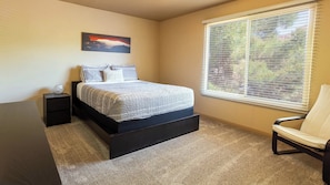 A bedroom with a bed, a nightstand, a chair, a window with blinds, and a painting on the wall.