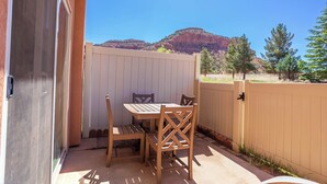 A patio with a table and chairs, a wooden fence, and a view of a mountain. - Kanab Retreat Near Zion w/ Pool & Hot Tub (Kanab)
