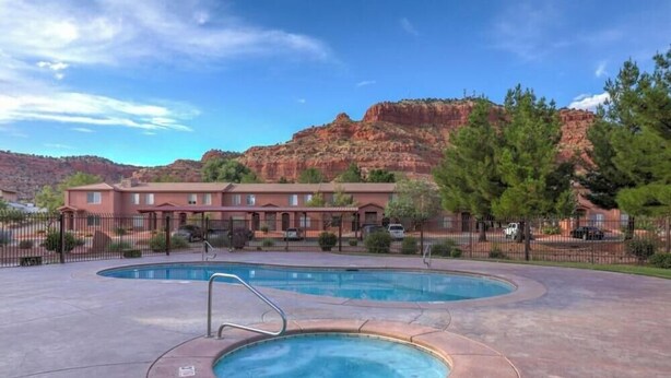 A hotel with a pool area, a mountain backdrop, and a fenced parking lot. - Kanab Retreat Near Zion w/ Pool & Hot Tub (Kanab)