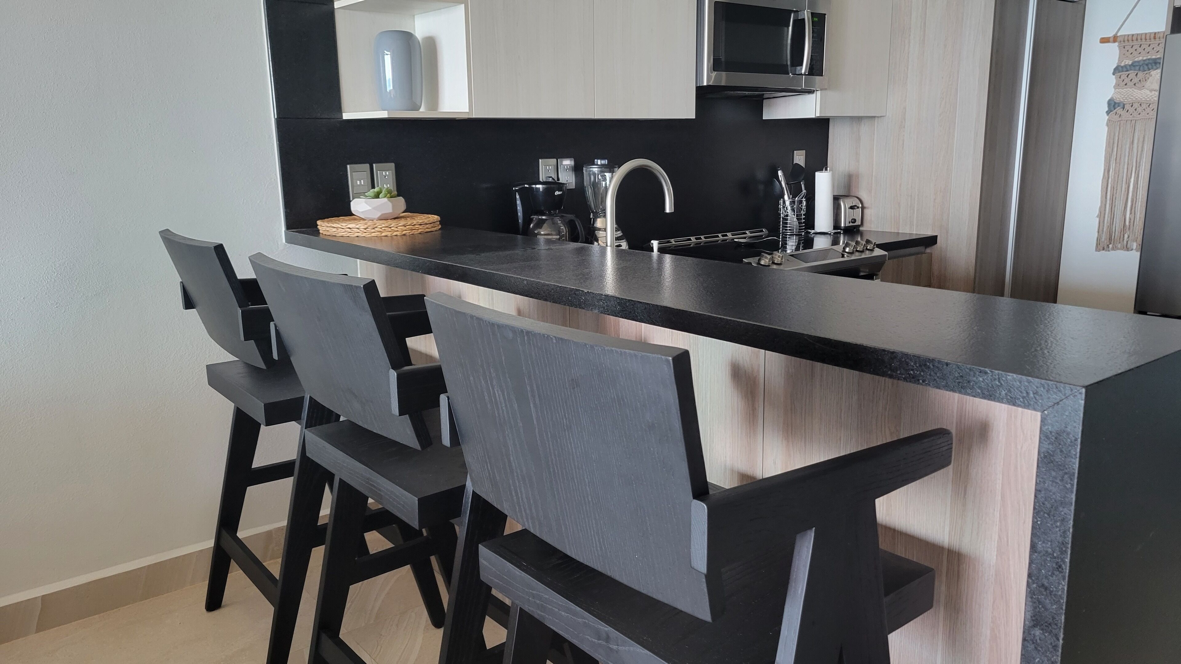 Une cuisine moderne dotée d’un plan de travail noir, d’appareils électroménagers en acier inoxydable et de trois chaises de bar noires.