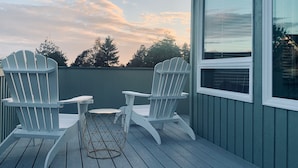 A deck with two Adirondack chairs and a small table, overlooking a green building with a window. - Beautiful Manzanita Getaway- Perfect for Family Large or Small - MCA #769 (Manzanita)