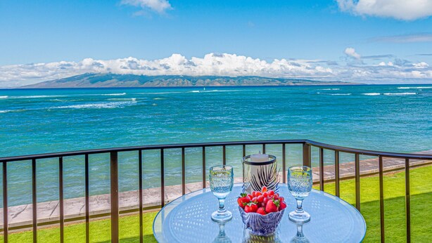 A balcony with a glass table, two glasses, a candle, and a bowl of strawberries. - Stunning Oceanfront Retreat, Kahana Reef 218  (Lahaina)