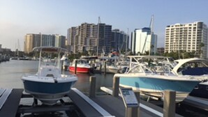 A marina with boats docked, a clear sky, and high-rise buildings in the background. - INCREDIBLE view of Palm Aire CC golf course from first floor Condo! (Sarasota)