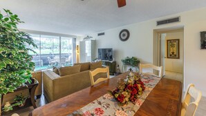A spacious living room with a dining area, large windows, and a ceiling fan. - INCREDIBLE view of Palm Aire CC golf course from first floor Condo! (Sarasota)