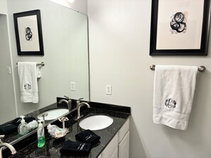 A bathroom with two sinks, a mirror, and towels with monogrammed towels.