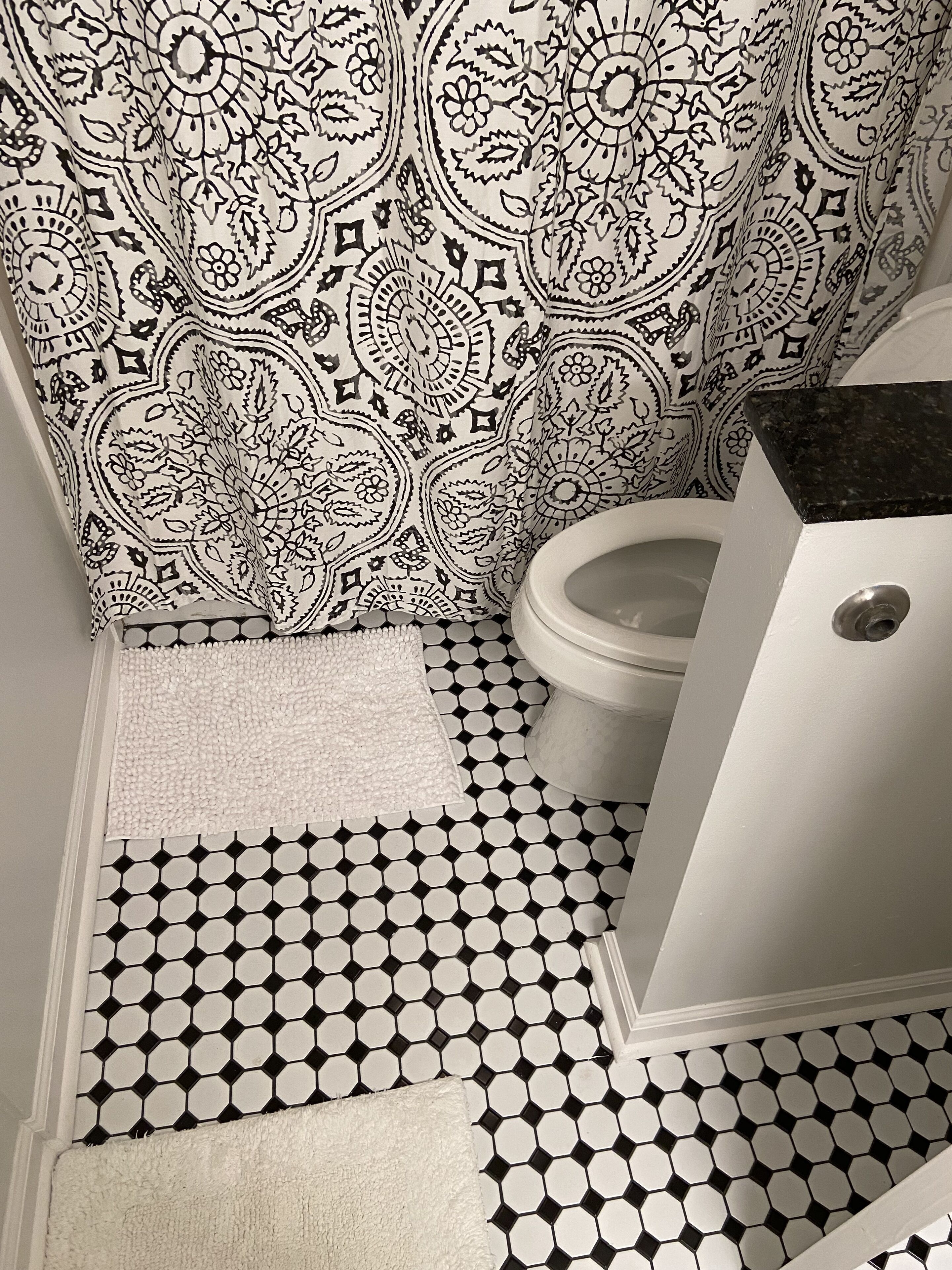 A bathroom with a patterned shower curtain, a toilet, and a tiled floor.