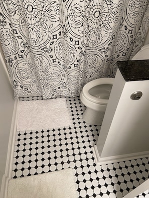 Un baño con cortina de ducha estampada, inodoro y piso de baldosas.