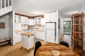 A compact kitchen with white cabinets, a built-in microwave, a refrigerator, and a wooden dining table. - Awesome North Shore Getaway Turtle Bay w/ pool, family safe beach, tennis, golf (Kahuku)