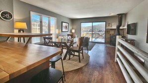 A modern dining area with a wooden table and chairs, a sofa, and a large window offering a view of a cityscape. - GREAT OLD TOWN LOCATION- SKI TO TOWN LIFT & STEPS TO MAIN ST!  (Park City)