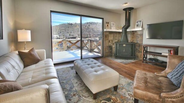 A living room with a sofa, ottoman, and armchair, a fireplace, and a large window with a view of a hilly landscape. - GREAT OLD TOWN LOCATION- SKI TO TOWN LIFT & STEPS TO MAIN ST!  (Park City)